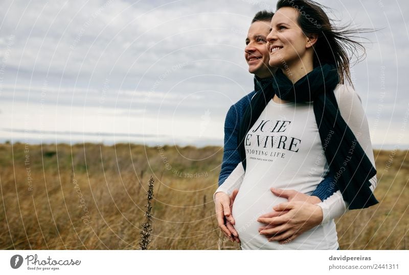 Pregnant with partner hugging and holding belly Lifestyle Happy Beautiful Human being Woman Adults Man Mother Couple Landscape Wind Grass Meadow Scarf Touch
