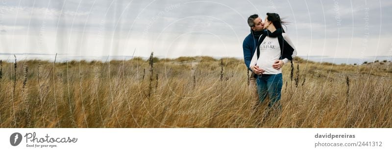 Pregnant with partner kissing and holding belly Lifestyle Human being Woman Adults Man Mother Couple Landscape Wind Grass Meadow Scarf Touch Kissing Love