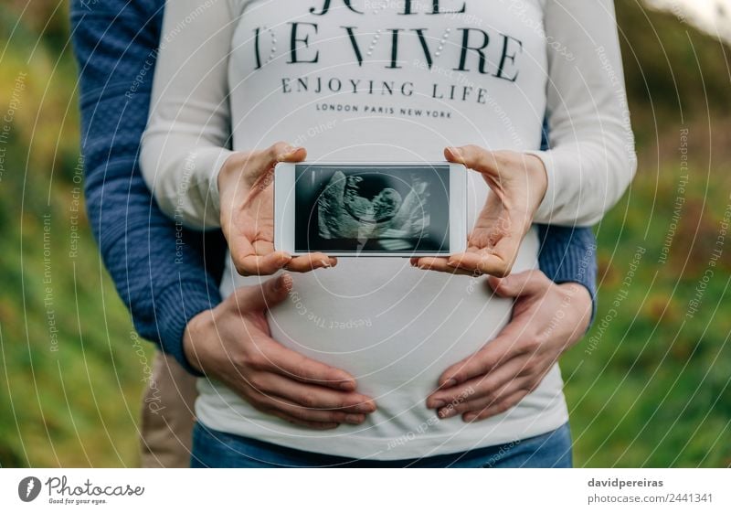 Pregnant showing ultrasound on the mobile with her partner Lifestyle PDA Technology Human being Baby Woman Adults Man Parents Mother Couple Hand Love Authentic