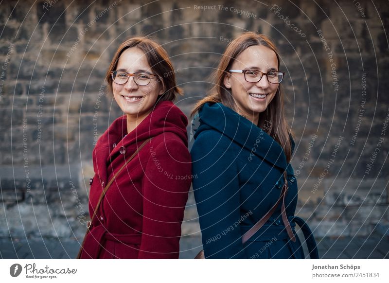 Twin sisters stand laughing back to back in front of a stone wall Lifestyle Style Joy luck Human being Feminine Young woman Youth (Young adults)