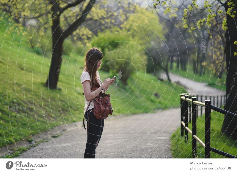 Attractive young woman having fun outside in a park. Caucasian girl with long brown hair checking her mobile Lifestyle Happy Beautiful Relaxation Calm