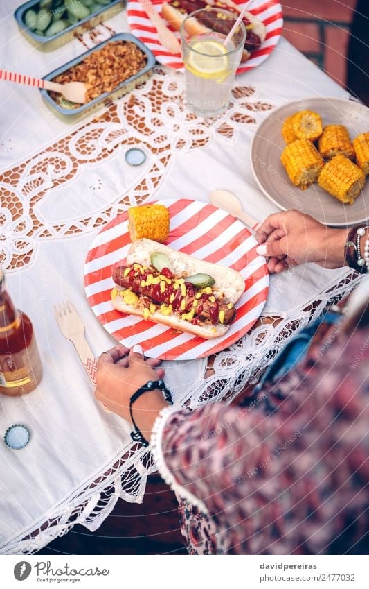 Woman holding plate with hot dog and corn Sausage Bread Roll Fast food Lemonade Alcoholic drinks Beer Plate Bottle Spoon Lifestyle Joy Happy Summer Table Adults