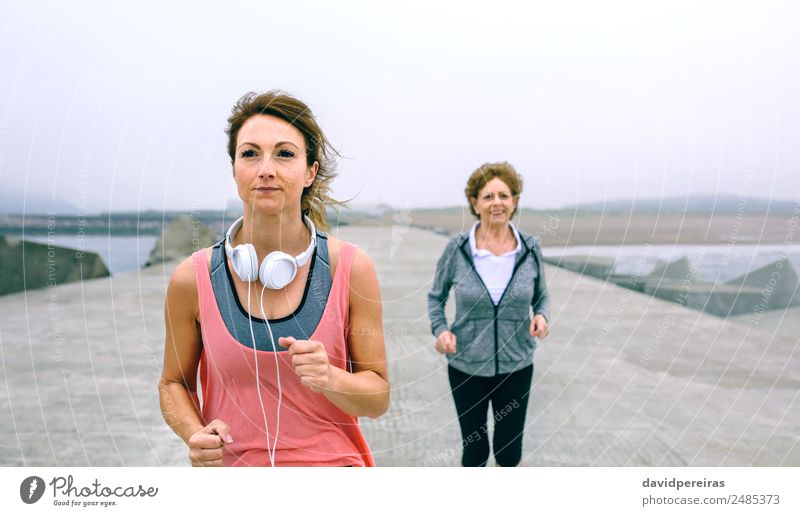 Young and senior sportswoman running by sea pier Lifestyle Wellness Ocean Sports Jogging Human being Woman Adults Mother Grandmother Fog Concrete Old Fitness
