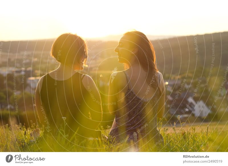 Sisters sitting on a meadow in the sunset Woman Love Happy Together Summer Joie de vivre (Vitality) Relaxation Friendship Attachment Rear view blurriness