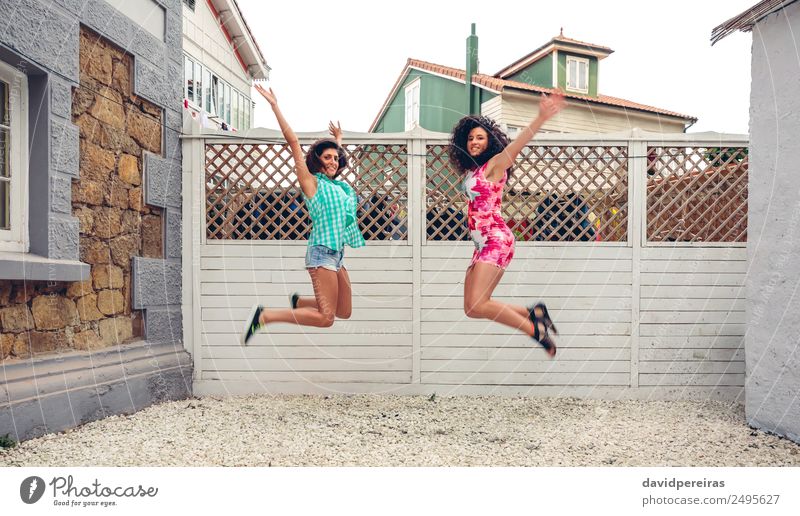 Happy women jumping in front of garden fence Lifestyle Joy Leisure and hobbies Summer Garden Human being Woman Adults Friendship Arm Brunette Wood To enjoy