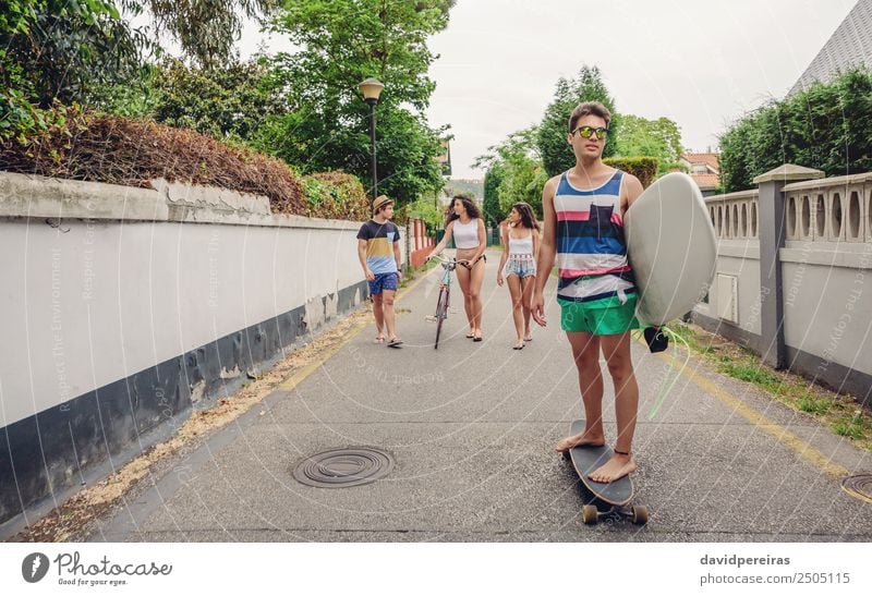 Young man riding on skate and holding surfboard Lifestyle Joy Happy Leisure and hobbies Summer Beach Sports Woman Adults Man Friendship Youth (Young adults)