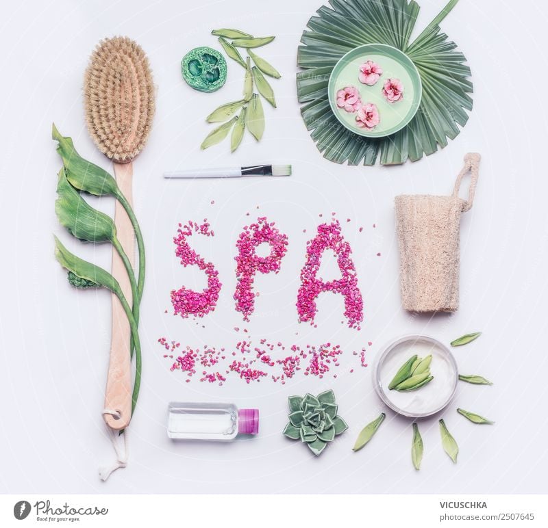 Spa or Wellness flat lay on white background. Body care and cellulite treatment tools. Natural brush for dry skin peeling or massage , cream and luffa sponge with flowers and tropical leaves, top view