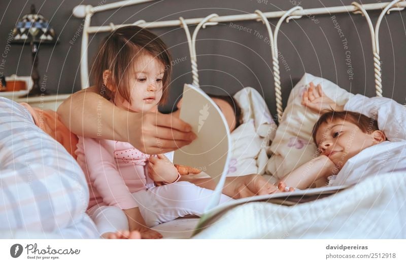 Baby girl reading book with family in the bed Lifestyle Joy Happy Beautiful Relaxation Leisure and hobbies Reading Bedroom Child Boy (child) Woman Adults