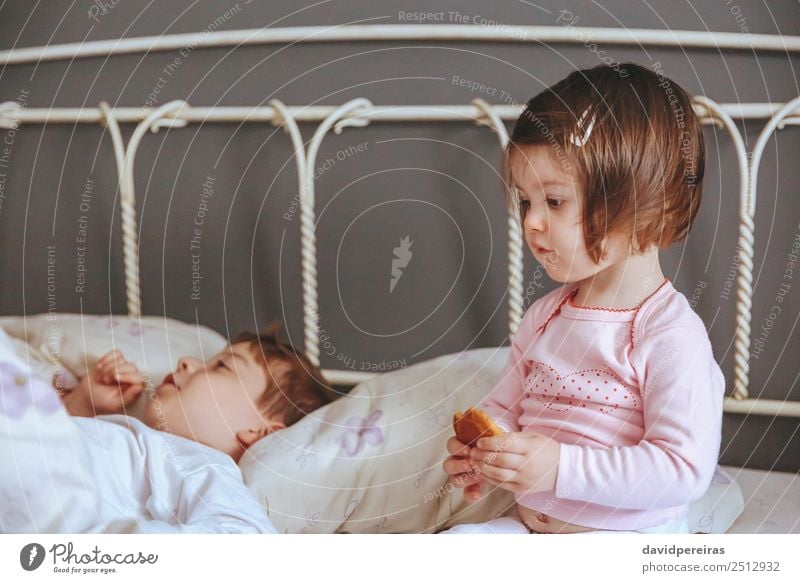 Little girl holding cookie sitting over the bed Eating Breakfast Lifestyle Joy Relaxation Leisure and hobbies Bedroom Child Baby Boy (child) Woman Adults