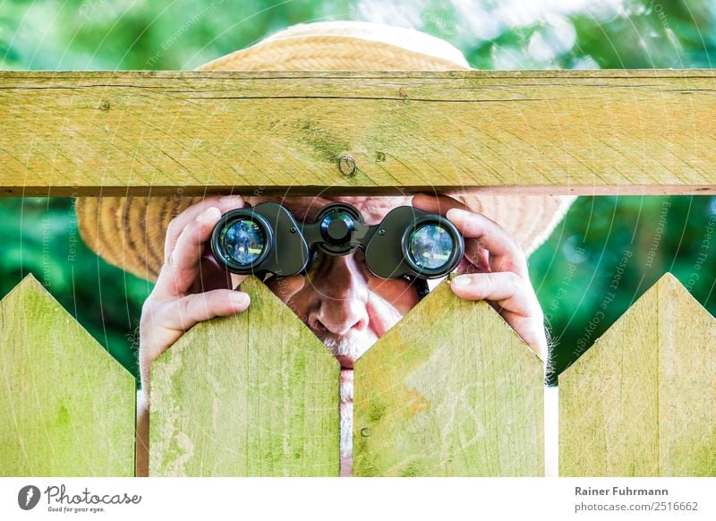 a curious neighbour observes with binoculars Human being Masculine Man Adults Male senior 1 Nature Garden Park Hat Straw hat Observe Threat Curiosity Discordant