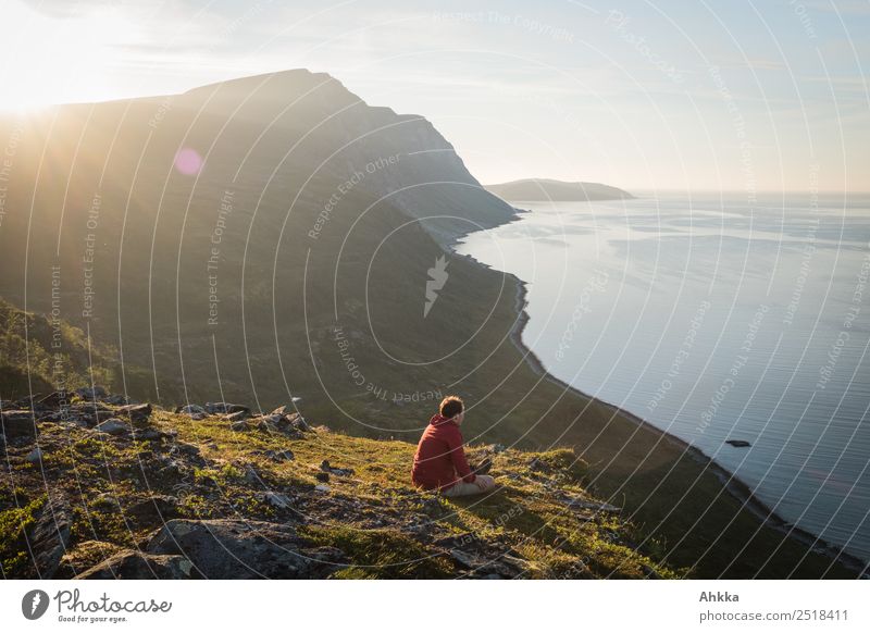 Man sitting on a cliff of a fjord with low sun on the European Arctic Ocean Back-light Cliff Fjord Sublime wide Reflection Small coast Sunlight Island Mountain