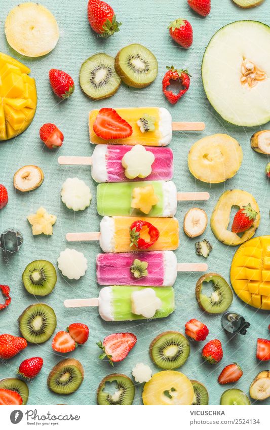 Colorful variety of Ice cream popsicles with fresh sliced fruits and berries ingredients on light blue background, top view, flat lay. Frozen tropical juices. Homemade ice cream lined up in a row