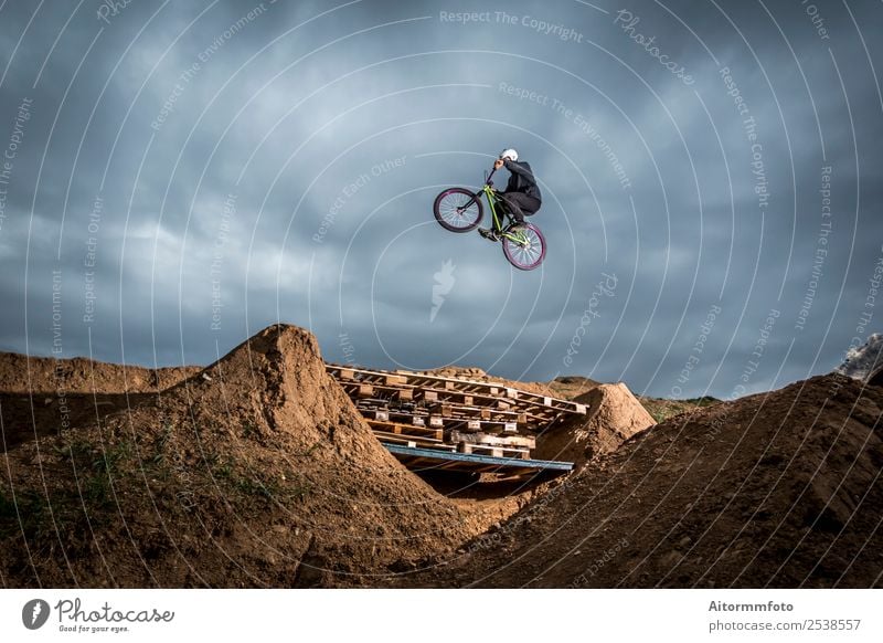 Young man jumping over hole in dirtjump circuit Joy Relaxation Mountain Sports Cycling Man Adults Nature Earth Clouds Park Hill Jump Speed Dangerous Acrobatics