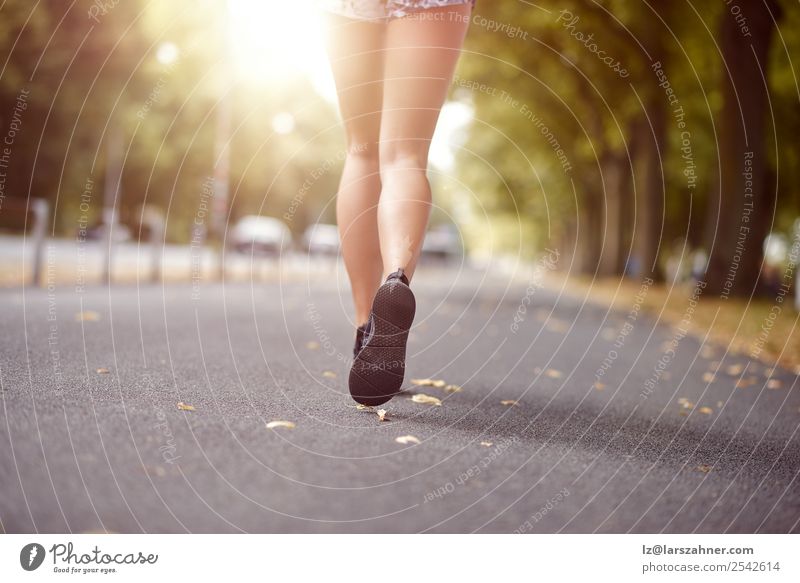 Young woman jogging down an autumn street Lifestyle Relaxation Summer Sun Sports Jogging Human being Woman Adults Feet Street Footwear Fitness Behind running