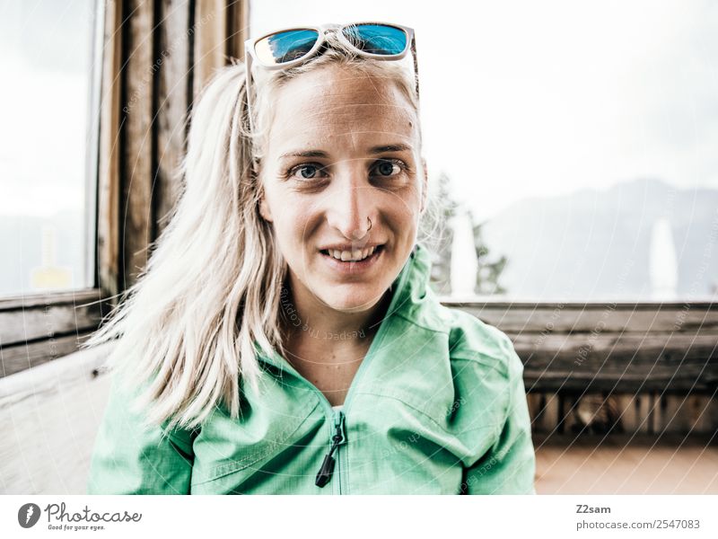 Young woman in a mountain hut Lifestyle Hiking Environment Nature Landscape Summer Beautiful weather Alps Mountain Track-suit top Sunglasses Blonde Braids