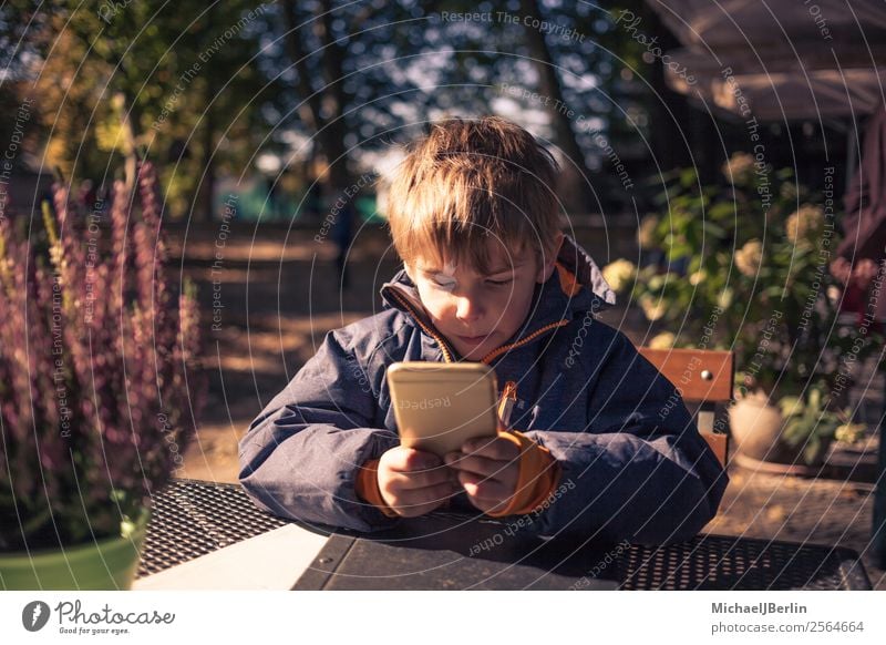 Boy sitting at outdoor table with smartphone Human being Masculine Child Boy (child) Infancy 1 3 - 8 years Autumn Playing Jacket Autumnal Cold Fresh