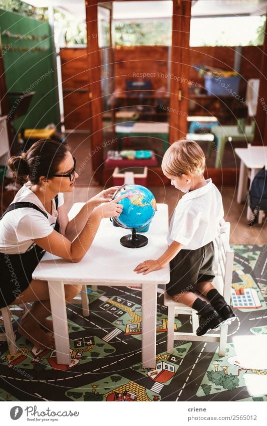 young boy studying with teacher in class room Happy Desk Child School Classroom Teacher Human being Boy (child) Woman Adults Man Book Globe Sit Small