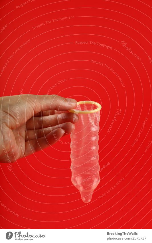 Close up woman hand holding condom over red Healthy Health care Medication Human being Woman Adults Man Hand Red Safety Protection Responsibility Caution Colour