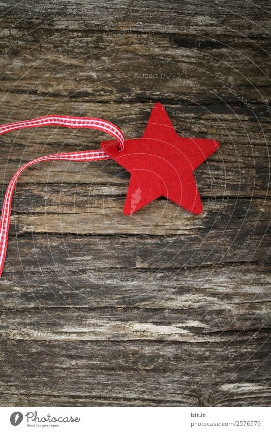 Merry Christmas. Red star of felt with ribbon, lies on old wood. Red checked Christmas star, as decoration on rustic brown wooden board. Felt fabric star as sign, blank, pendant, hanger on brown, rustic wooden table, text space.
