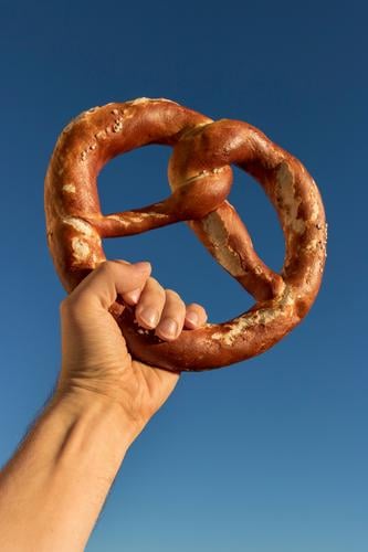 Long live the pretzel. Dough Baked goods Bread Feasts & Celebrations Oktoberfest Man Adults Hand Fingers Sky Cloudless sky Select To hold on To enjoy