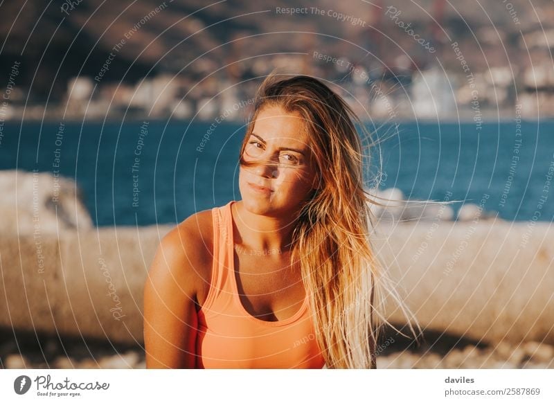 Beautiful woman with sports clothes, sitting on a concrete wall outdoors at sunset. Lifestyle Body Leisure and hobbies Sun Ocean Sports Fitness Sports Training