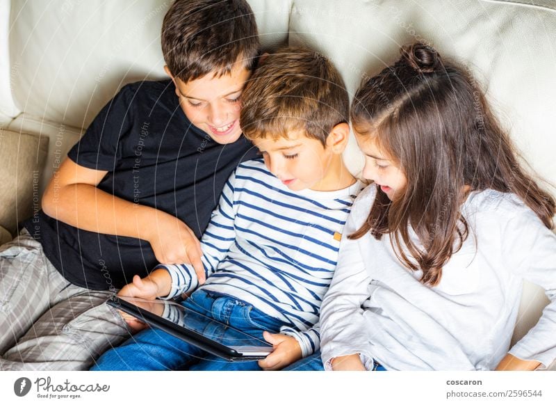 Three kids using a tablet at home Lifestyle Joy Happy Beautiful Leisure and hobbies Playing Reading Sofa Child Cellphone Games console Computer Notebook Screen