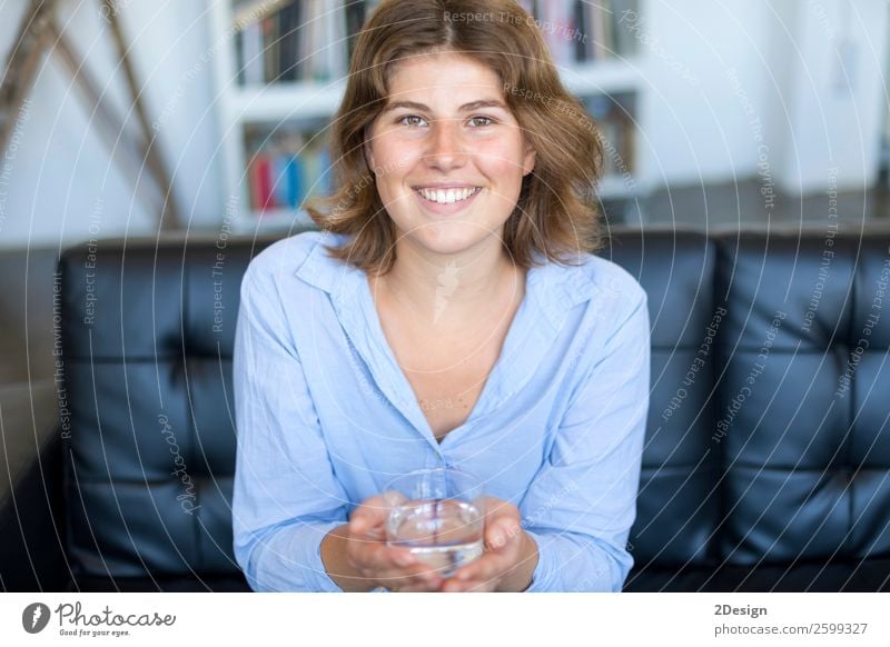 Front view portrait of a happy teen holding a glass of water Diet Beverage Drinking Lifestyle Happy Beautiful Face Wellness Sofa Camera Feminine Young woman