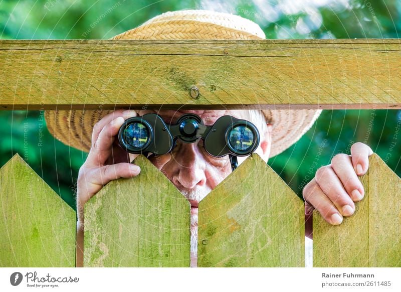 a man looks through a fence with binoculars Human being Masculine Man Adults Male senior 1 "Fence Paling fence" Hat Binoculars Observe Curiosity Grouchy