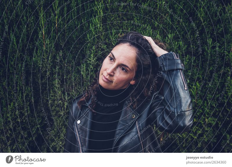 Woman wearing a leather jacket against a cypress wall. Lifestyle Happy Beautiful Face Human being Nature Plant Autumn Park Fashion Jacket Leather Brunette Touch