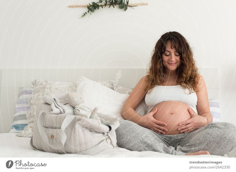 Happy pregnant woman sitting and touching her belly at home Lifestyle Beautiful Leisure and hobbies Sofa Human being Baby Woman Adults Parents Mother