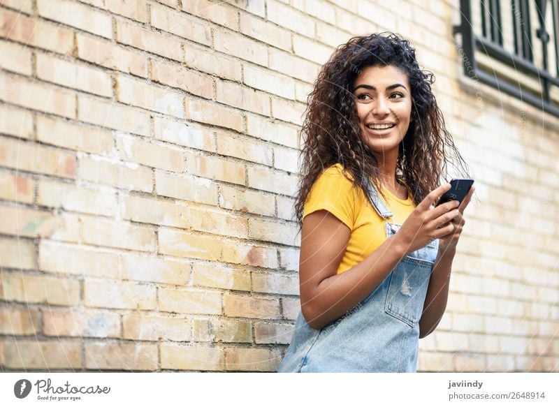 Happy Arab girl using smart phone on brick wall. Lifestyle Style Beautiful Hair and hairstyles Telephone PDA Technology Human being Feminine Young woman