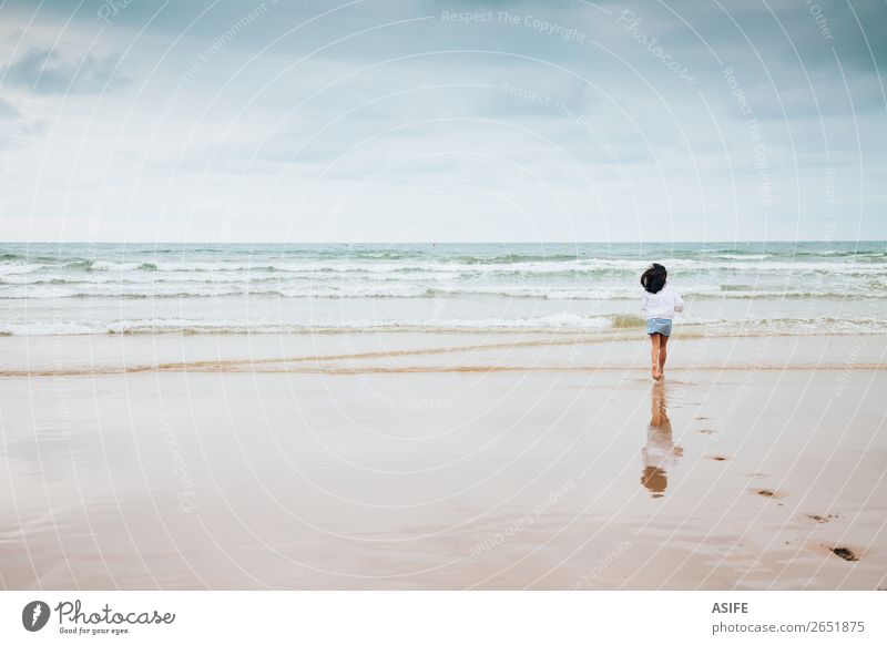 Girl enjoying the beach with bad weather Joy Beach Ocean Waves Sports Child Infancy Nature Landscape Sand Sky Clouds Bad weather Footprint To enjoy Jump Wet