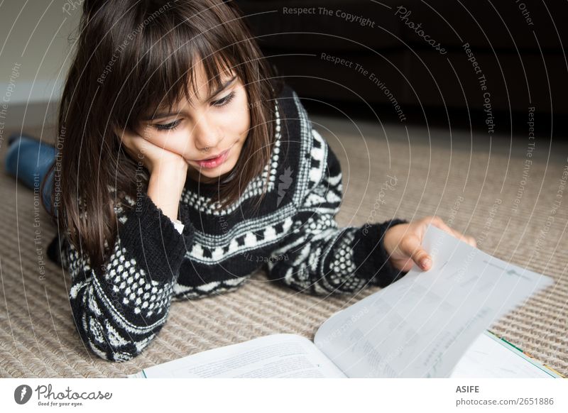 Cute little girl lying on the carpet reading a book Lifestyle Joy Happy Beautiful Relaxation Leisure and hobbies Reading Child School Human being Woman Adults