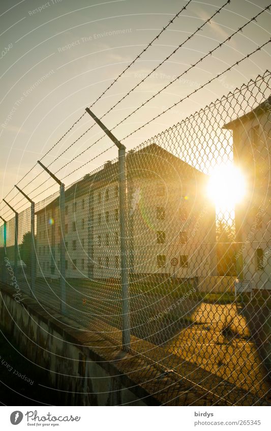 Barracks or housing complex fenced with fence and barbed wire in the backlight of the evening sun barracks Residential complex Safety Fence Barbed wire