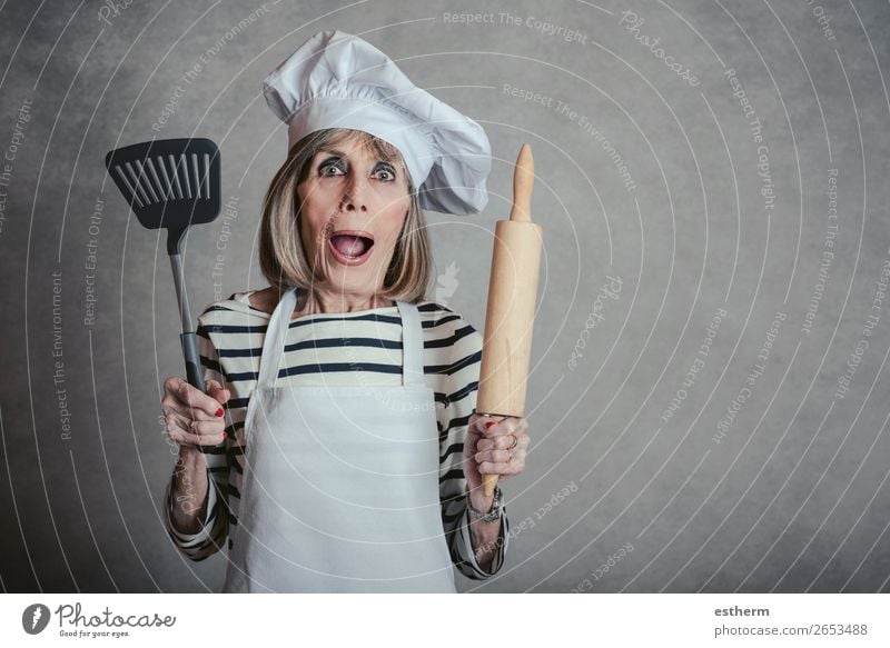 senior woman with cook hat and rolling pin and spatula on gray background Nutrition Diet Lifestyle Leisure and hobbies Kitchen Restaurant Retirement Feminine