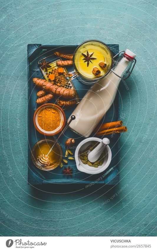 Healthy golden turmeric milk on tray with ingredients: cardamom, turmeric, cinnamon, honey and ginger on blue background , top view, vertical.  Immune boosting remedy , detox and dieting concept.