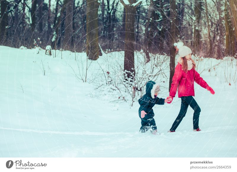 Teenage girl enjoying snow with her little sister. Children are walking through deep snow while snow falling, enjoying wintertime. Sisters spending time together. Girls are wearing winter clothes, young girl is wearing pink coat and wool cap