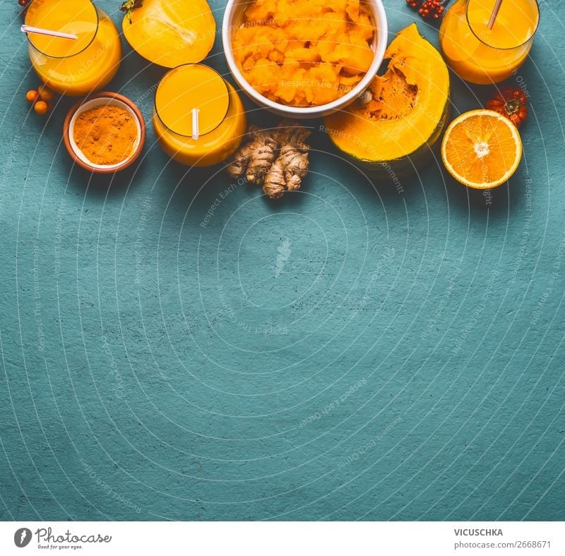 Healthy pumpkin smoothie in glasses with orange color ingredients : persimmon , orange fruits, ginger and turmeric powder on blue background, top view. Immune boosting detox beverage for cold season