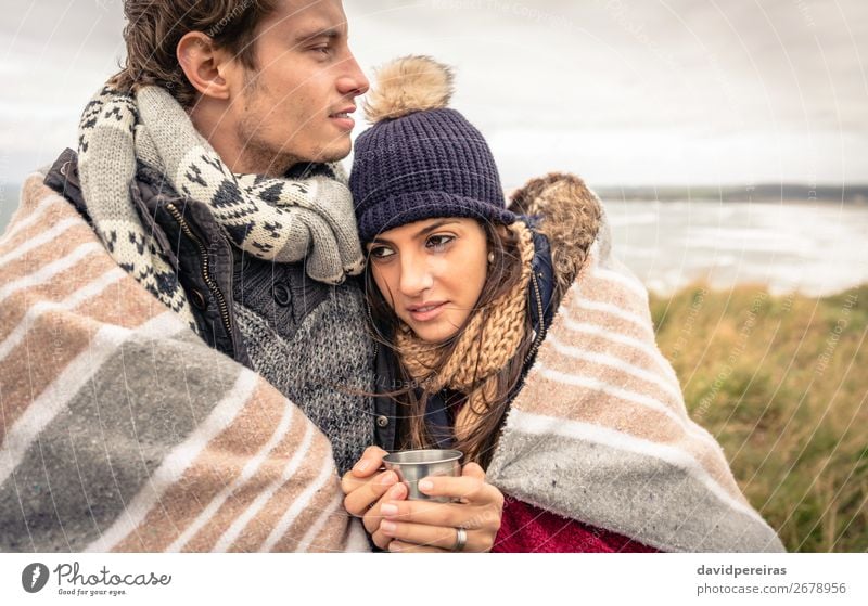 Young couple embracing outdoors under blanket in a cold day Beverage Coffee Tea Lifestyle Happy Ocean Winter Mountain Woman Adults Man Couple Nature Sky Clouds