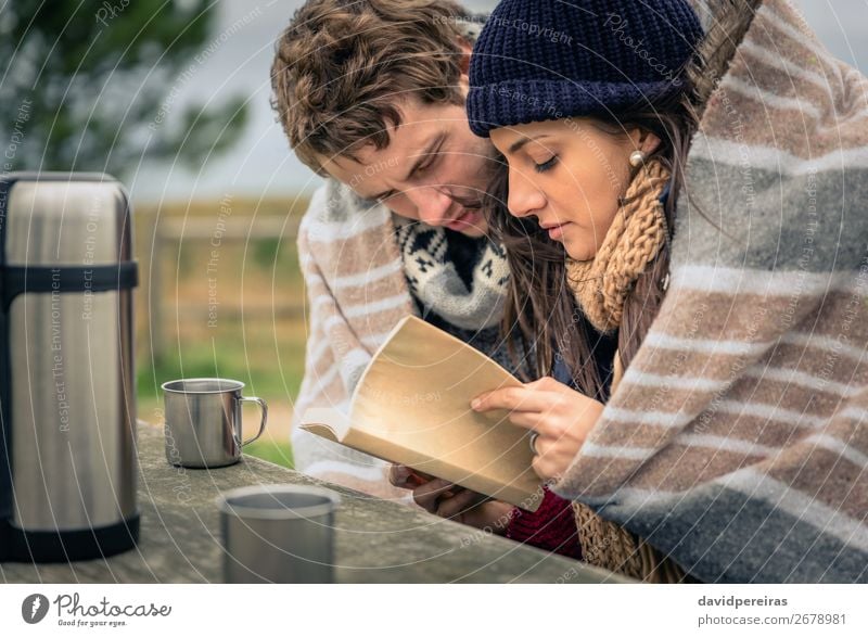 Young couple under blanket reading book outdoors in a cold day Beverage Coffee Tea Lifestyle Reading Adventure Winter Mountain Table Woman Adults Man Couple