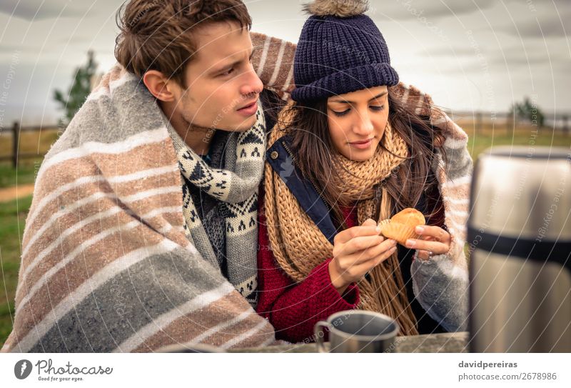 Young beautiful couple under blanket eating muffin with dark cloudy sky on background Eating Beverage Coffee Tea Lifestyle Happy Ocean Winter Table Woman Adults