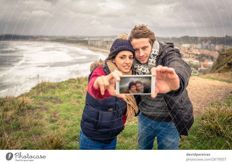 Couple taking selfie photo in smartphone with sea and dark cloudy sky on background Lifestyle Happy Beach Ocean Winter Telephone PDA Camera Woman Adults Man