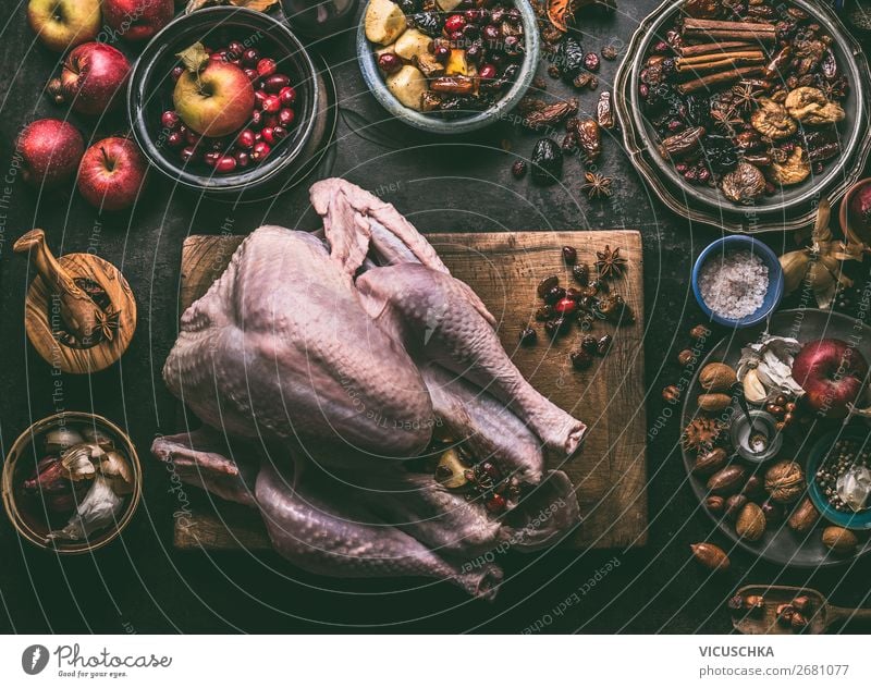 Raw whole turkey stuffed with dried fruits and apples on wooden cutting board, dark kitchen table background with ingredients , top view. Cooking preparation for Thanksgiving or Christmas dinner.