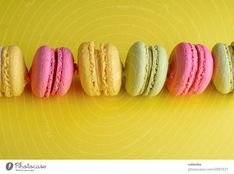 dessert macarons lies in a row in the middle Cake Dessert Candy Bright Yellow Green Pink Colour Almond background Baking Bakery biscuit colorful cream