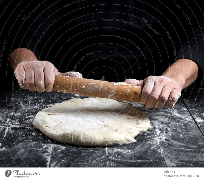 chef in a black tunic rolls a dough for a round pizza Dough Baked goods Bread Nutrition Table Kitchen Cook Man Adults Hand Wood Make Fresh White Rolling pin