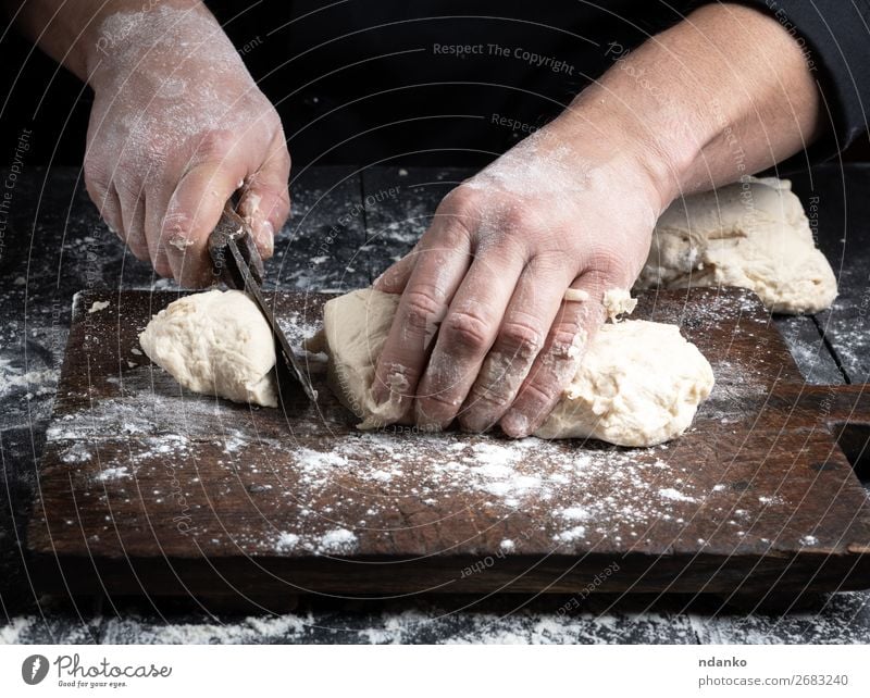 chef cuts white wheat flour dough into pieces Dough Baked goods Bread Nutrition Table Kitchen Cook Human being Man Adults Hand Wood Make Black White Tradition