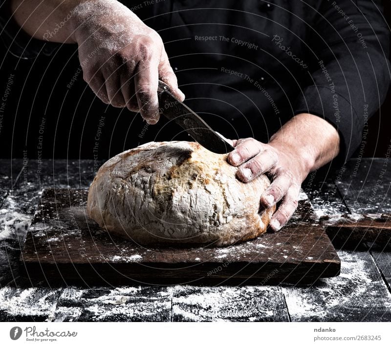 man cuts with a knife a round whole loaf Bread Nutrition Knives Table Kitchen Human being Hand Fingers Wood Make Dark Fresh Brown Black White Tradition Baking