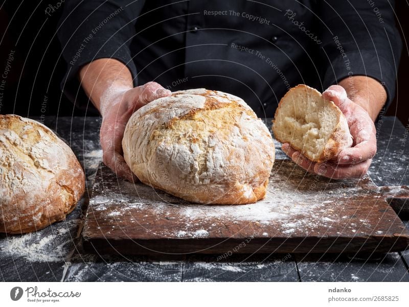 cook in a black tunic holds fresh baked bread Bread Nutrition Table Kitchen Human being Hand Fingers Wood Make Dark Fresh Brown Black White Tradition Baking