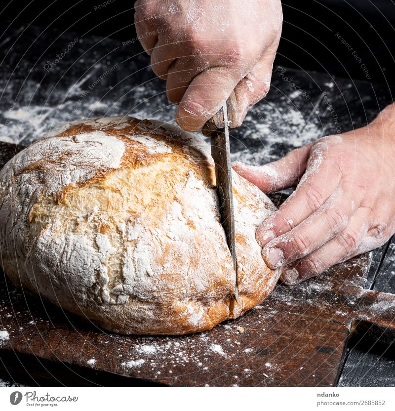 male hands cut a knife round baked bread Bread Nutrition Knives Table Kitchen Human being Hand Fingers Wood Make Dark Fresh Brown Black White Tradition Baking