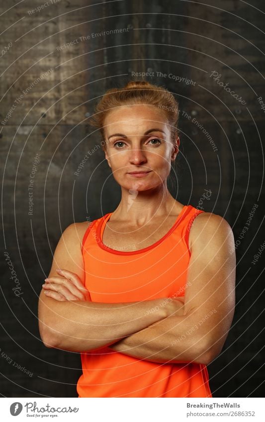 Close up front upper body portrait of one young athletic woman in sportswear in gym over dark background, looking at camera and smiling Lifestyle Sports Fitness